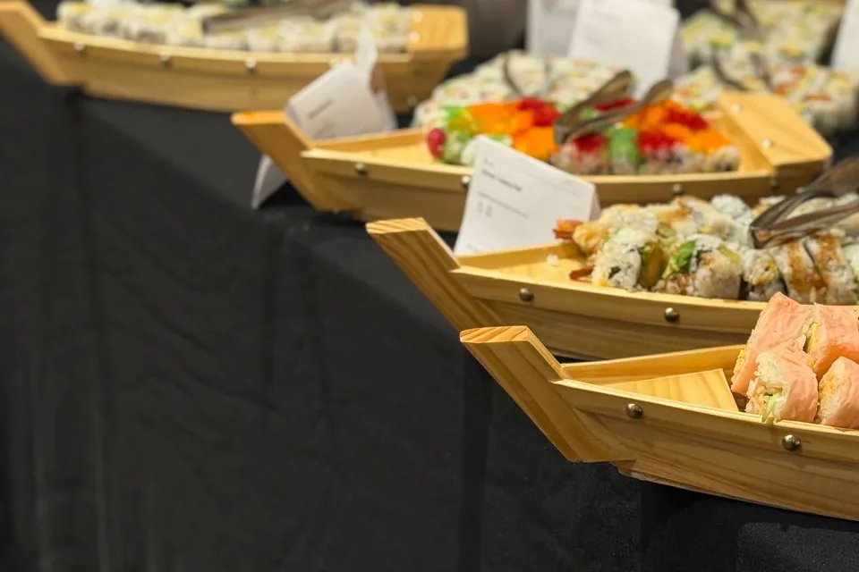 Wooden sushi boats filled with assorted rolls receding down a black-linen office buffet line in Seattle