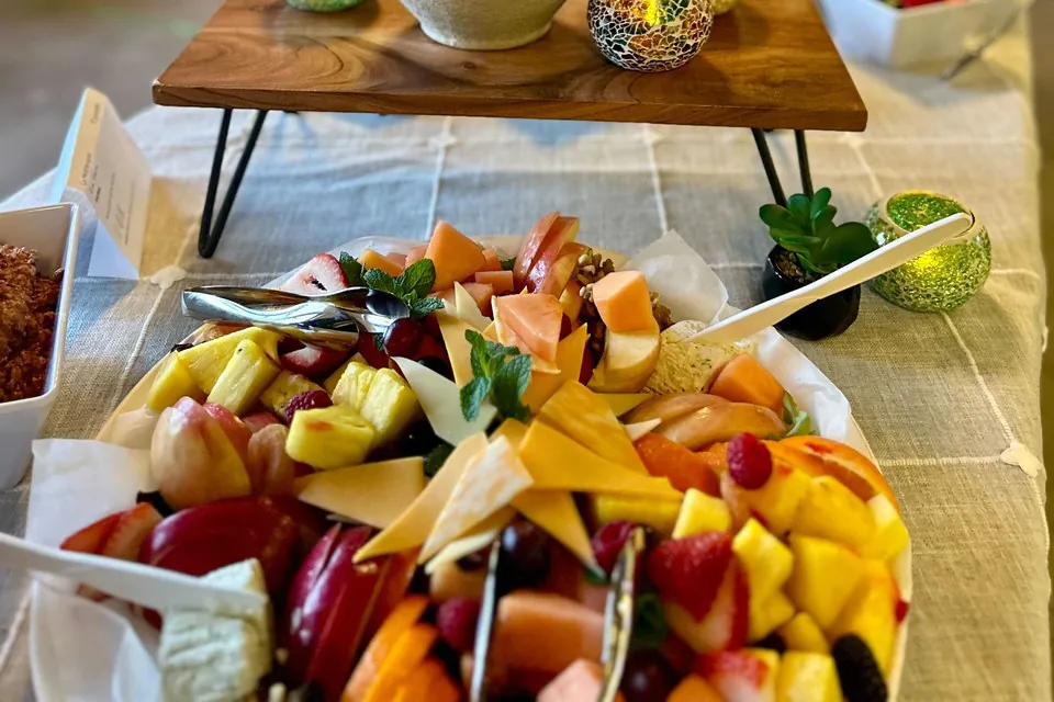 Fresh summer fruit and cheese platter with melon, pineapple, peaches, berries, mint, and cheese wedges on an office catering table