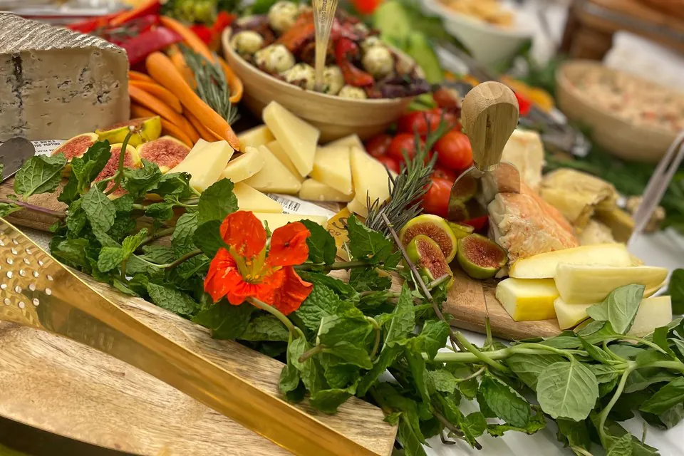Summer grazing board with hard cheeses, carrots, figs, marinated mozzarella, cherry tomatoes, fresh herbs, and a bright orange nasturtium flower