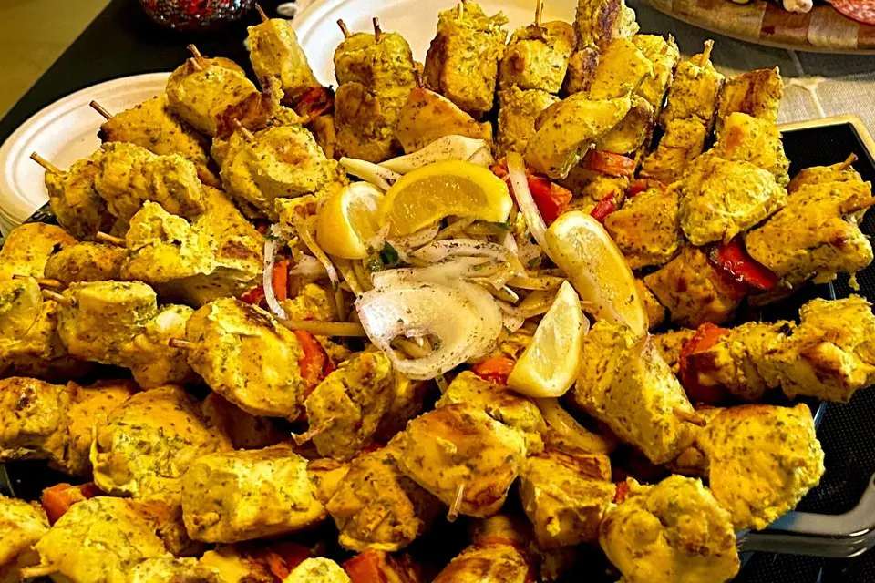 Platter of grilled chicken skewers with lemon wedges, onions, and peppers at a summer office catering buffet