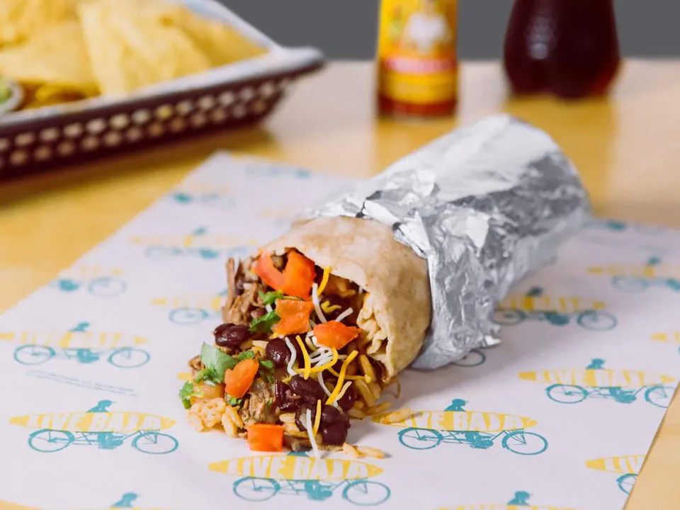 A foil-wrapped burrito opened to show carnitas, rice, black beans, cheese, and pico de gallo on Taco del Mar branded paper