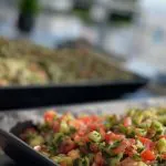 Office catering buffet with black trays of fresh chopped Israeli salad and tabbouleh by a window with a city skyline