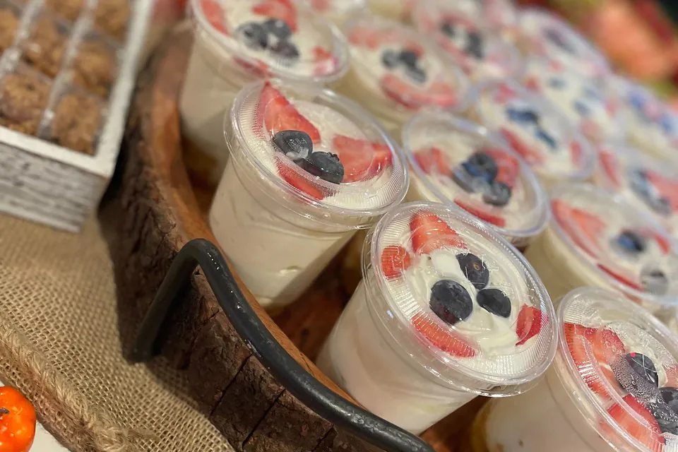 Rows of individual yogurt-and-fresh-fruit parfait cups topped with sliced strawberries and blueberries on a wood serving board, a grab-and-go fresh catering option