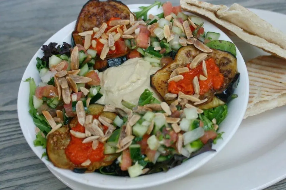 Bite NYC Mediterranean salad Bite Mediterranean salad plate with hummus, roasted eggplant, red pepper tapenade, Middle Eastern chopped salad, toasted almonds and pita
