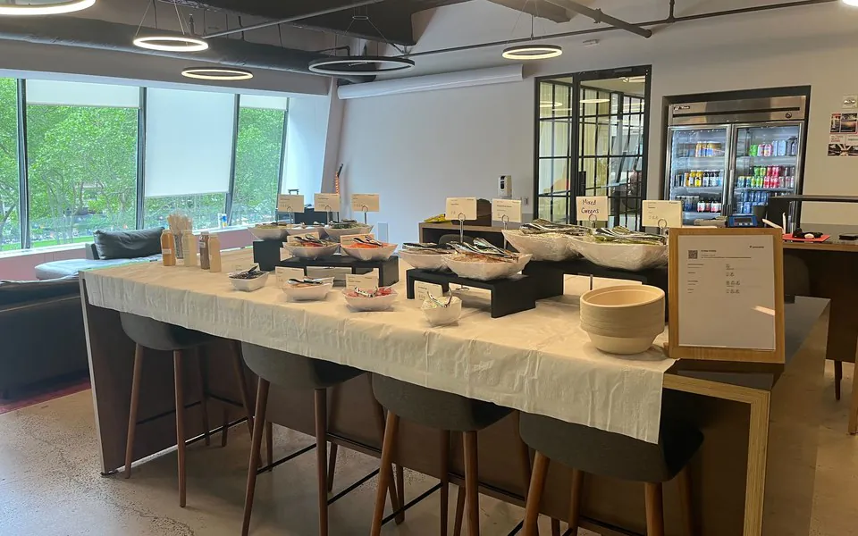 Build-your-own office bowl bar with labeled white bowls of greens, grains, and toppings on a linen-draped table