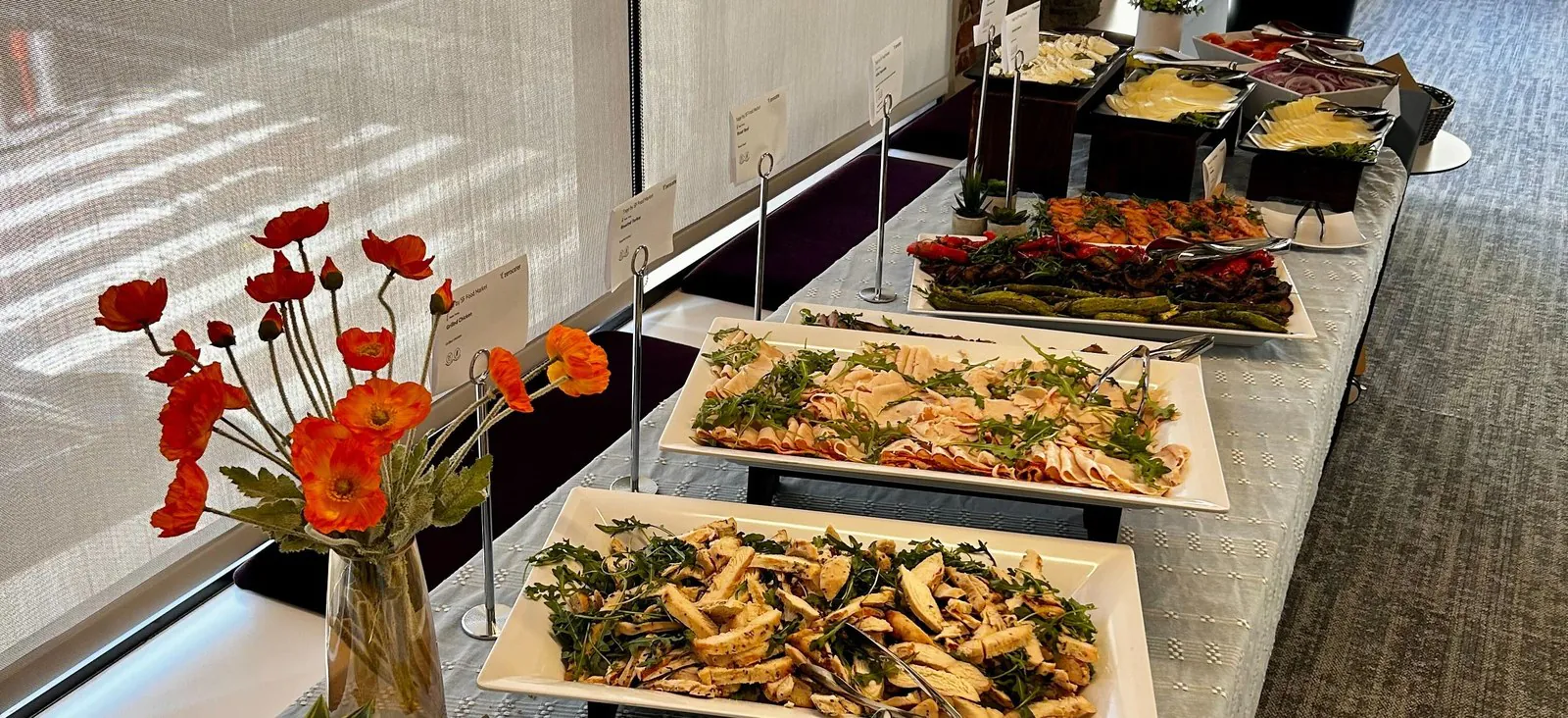 Fresh Mediterranean office catering buffet with platters of sliced grilled chicken, deli meats, roasted vegetables, and dips