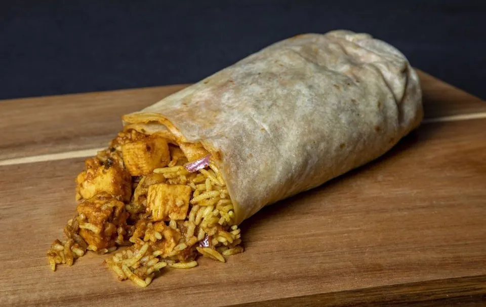 Curry Up Now paneer tikka masala burrito Curry Up Now paneer tikka masala burrito cut open to show turmeric rice and paneer in a flour tortilla