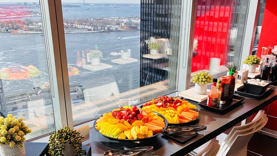 Fruit platters set on a high-rise office counter beside floor-to-ceiling windows overlooking the harbor for a pre-market breakfast