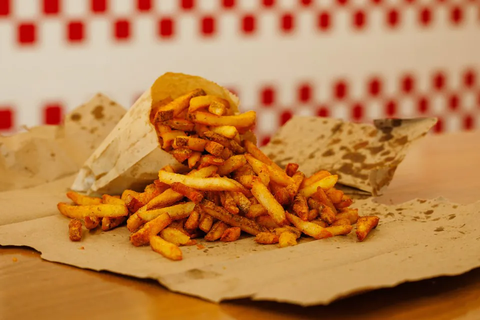 Cajun-seasoned fresh-cut Five Guys fries spilling from a kraft paper bag onto brown paper against a red and white checkered wall