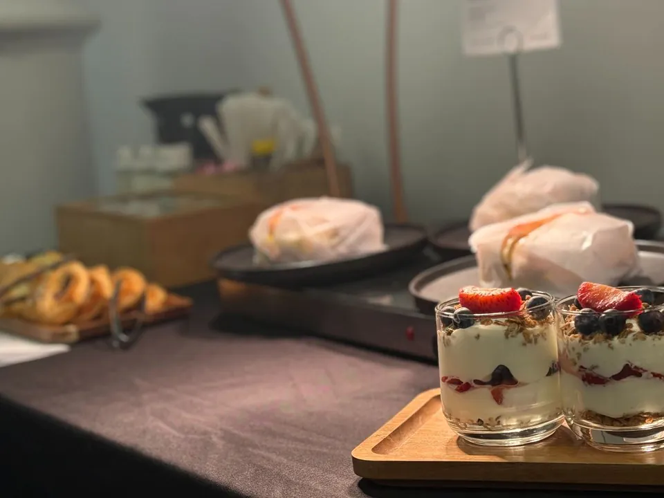 Yogurt parfait cups layered with granola, strawberries, and blueberries on a wooden tray at an office breakfast