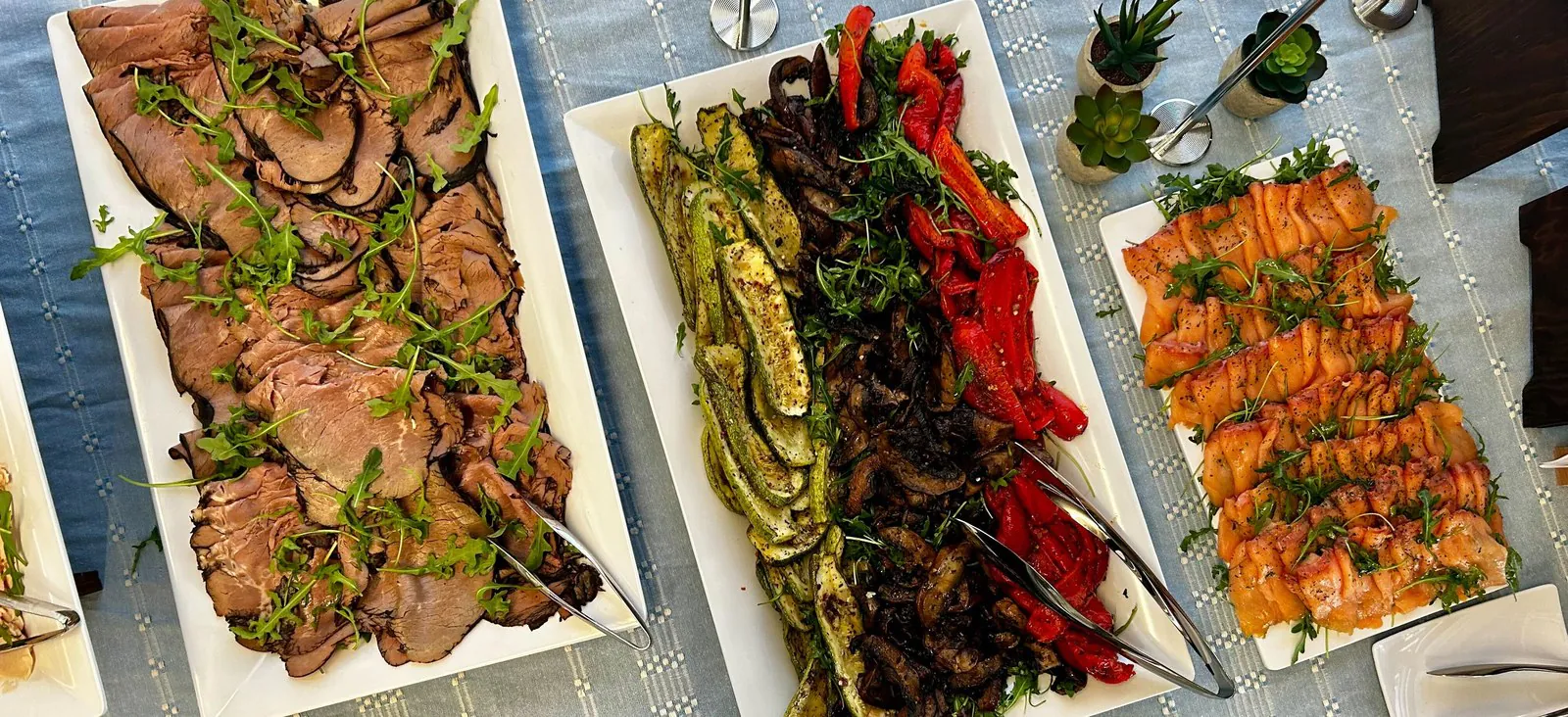 Overhead platters of sliced roast beef, grilled zucchini, mushrooms and peppers, and smoked salmon, a protein-forward keto office catering spread
