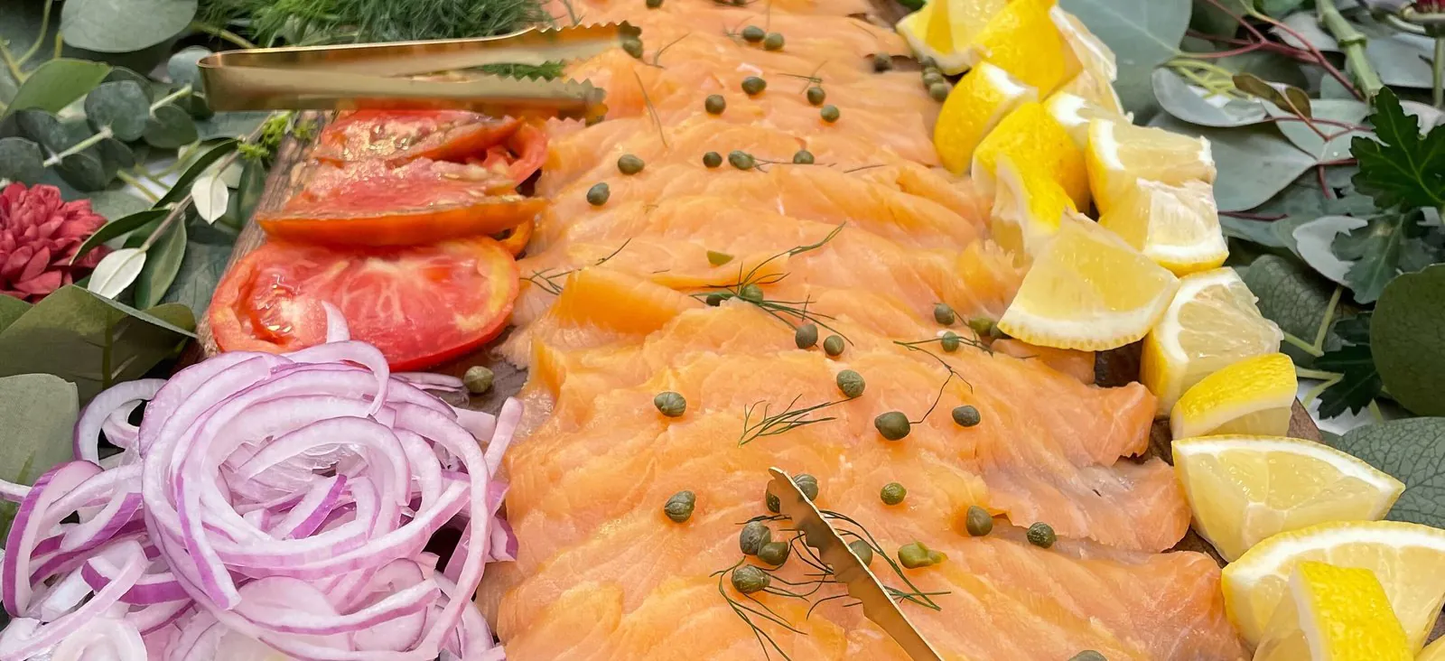 Smoked salmon lox board with capers, dill, red onion, sliced tomato and lemon wedges, a pareve fish centerpiece for kosher office catering