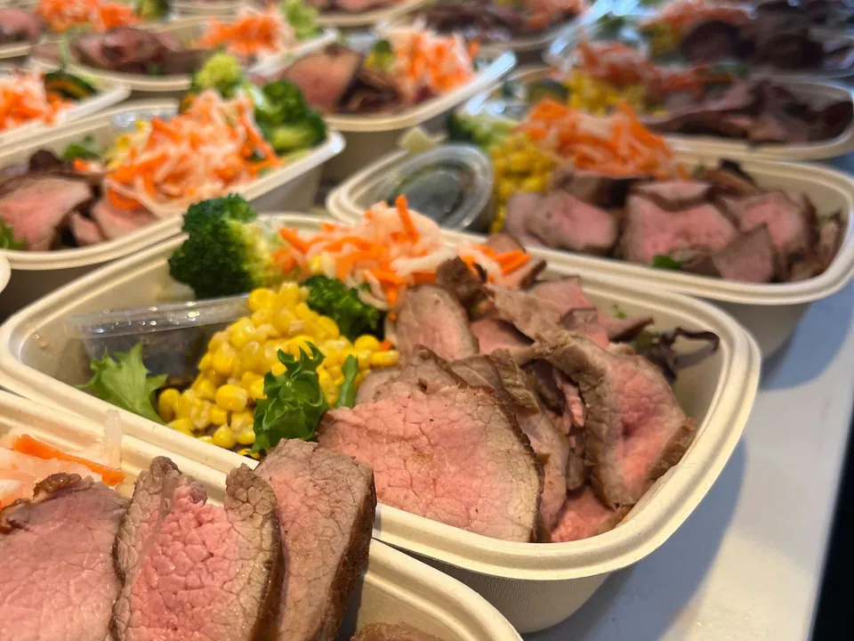 Rows of hearty boxed meals with sliced roast beef, corn, broccoli, and slaw ready for a shift crew to grab