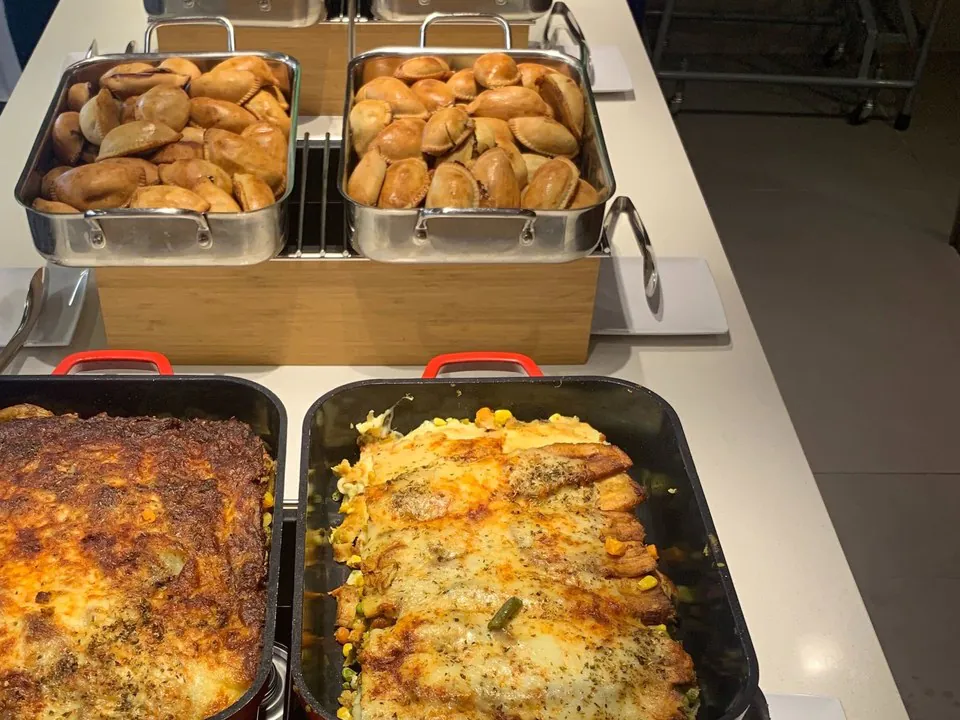 Budget-friendly buffet of baked casseroles in red pans and trays of golden empanadas set up for a volunteer crew