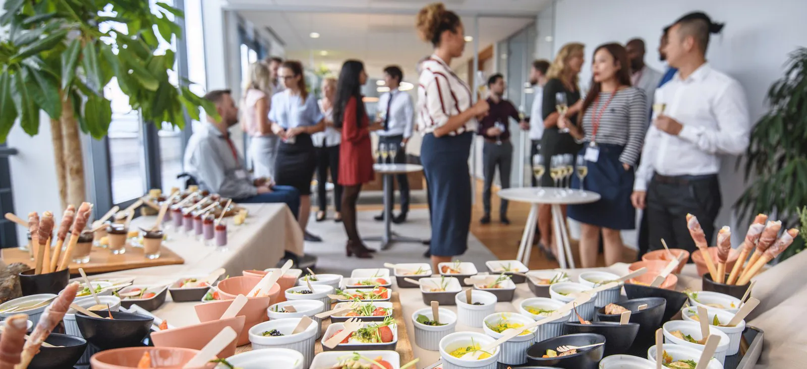 Reception spread of small-plate ramekins on a table with donors mingling and holding drinks in the background
