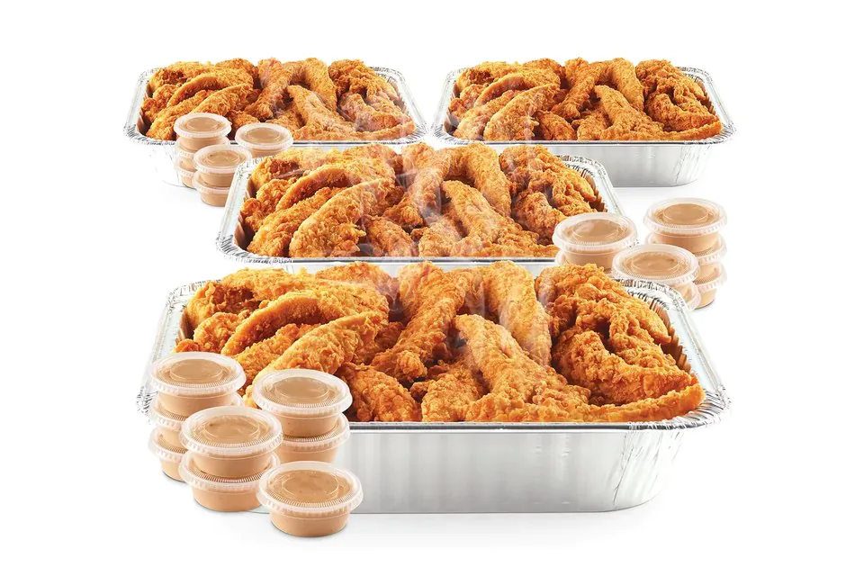 Four foil catering trays of Raising Cane's chicken fingers stacked in depth with rows of Cane's Sauce cups in front of them