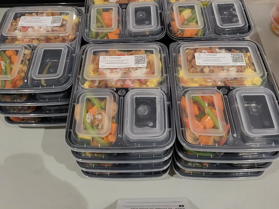 Stacks of individually boxed office lunches with grilled protein and vegetables, each labeled and sealed