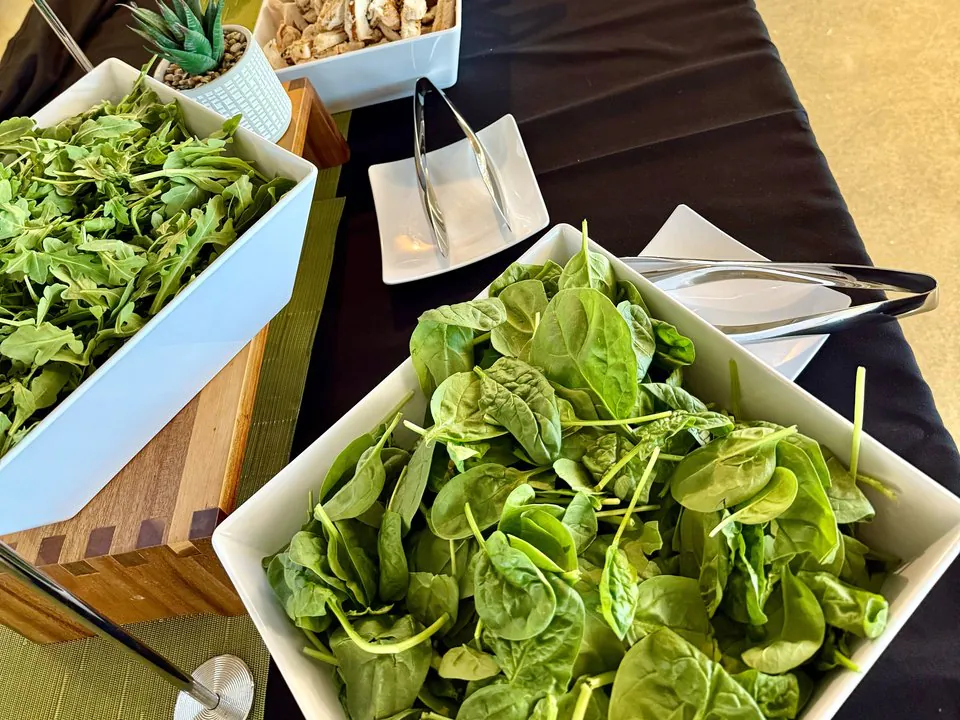 Fresh office salad bar with bowls of spinach, arugula, grilled chicken, and toppings on a black-draped counter