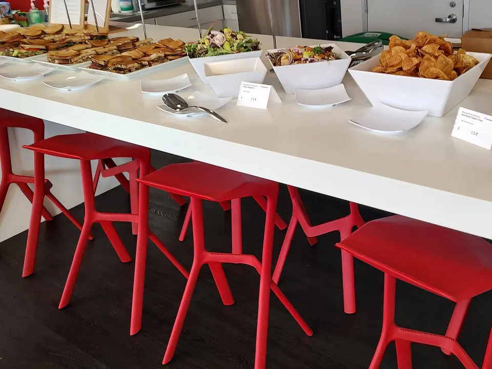 Office sandwich spread with quartered gourmet sandwiches, two side salads, and a bowl of kettle chips on a white counter