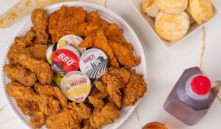 Bojangles catering bundle with bone-in chicken and tenders on a platter, four dipping sauce cups, a tray of biscuits and a half gallon of iced tea