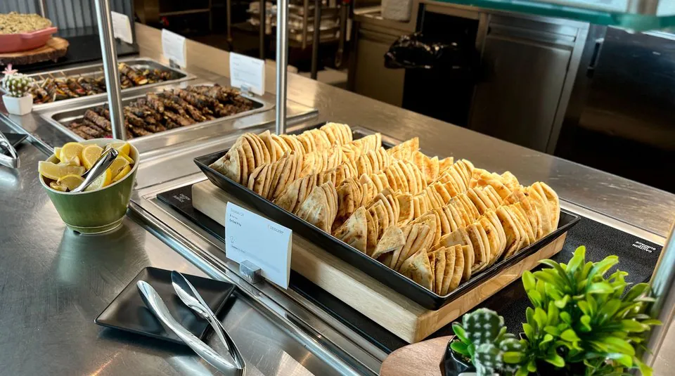 Grilled pita triangles fanned in overlapping rows across a black tray on a wooden board, with skewers and lemon wedges behind