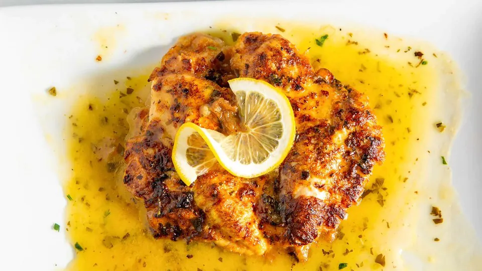 Chicken francese in lemon butter sauce topped with lemon slices and chopped parsley on a white plate