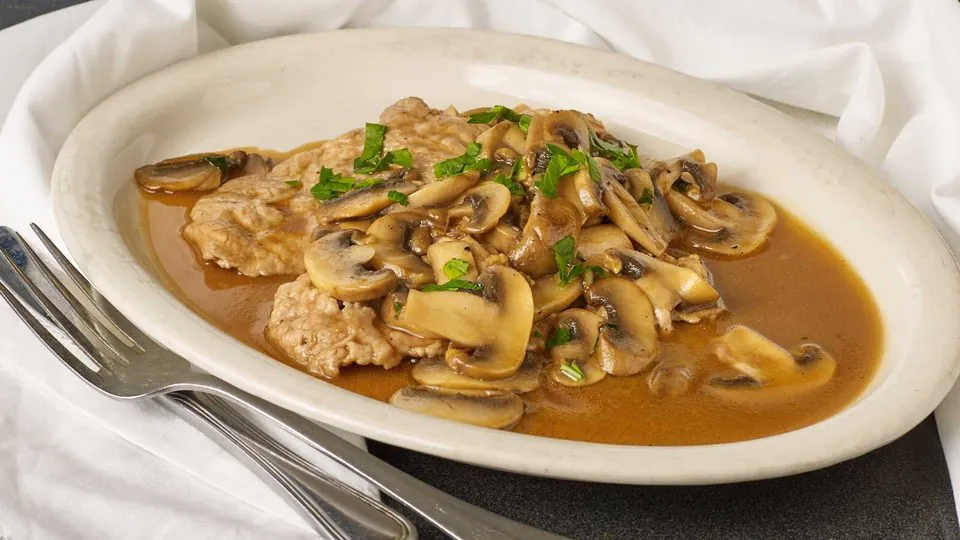 Veal marsala with sliced mushrooms in brown marsala sauce on an oval white platter with a linen napkin