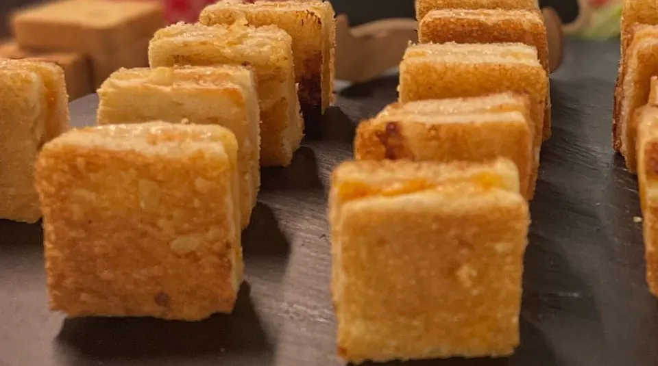 Grilled cheese cut into small cubes and stood on end across a round slate platter at an office reception