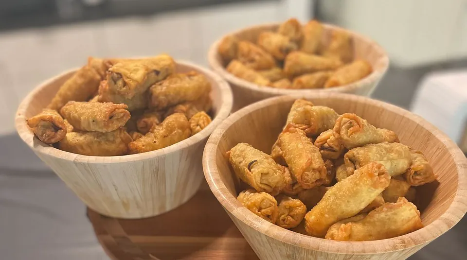 Three bamboo bowls of crisp egg rolls arranged on a tiered wooden stand over black linen