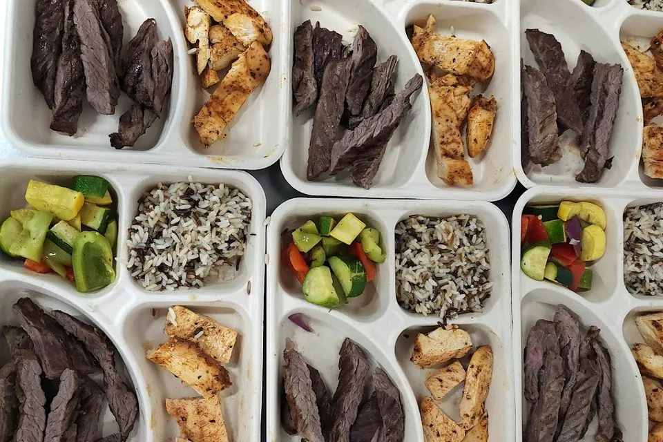 Individual compartment trays of grilled steak, grilled chicken, wild rice, and sauteed vegetables with no sauces or butter finish