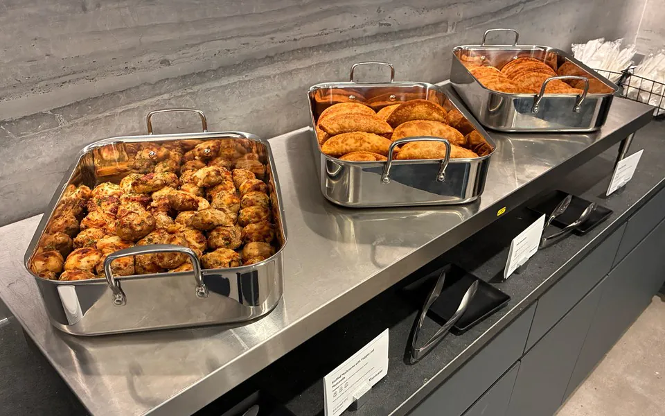Stainless hotel pans of fried chicken and hand pies lined up on a steel counter for an office catering line