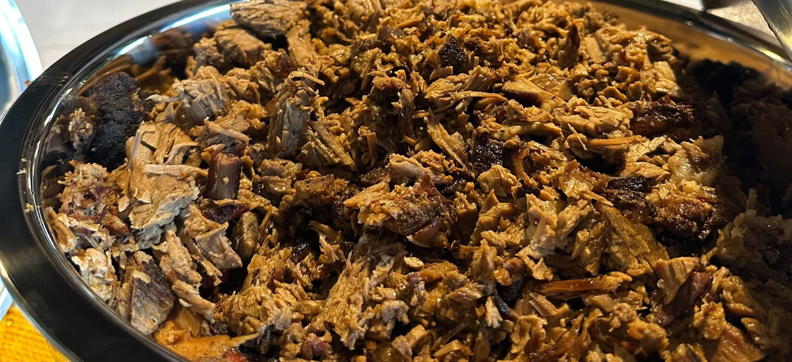 Chopped hickory-smoked brisket filling a stainless chafing dish at an office barbecue catering buffet