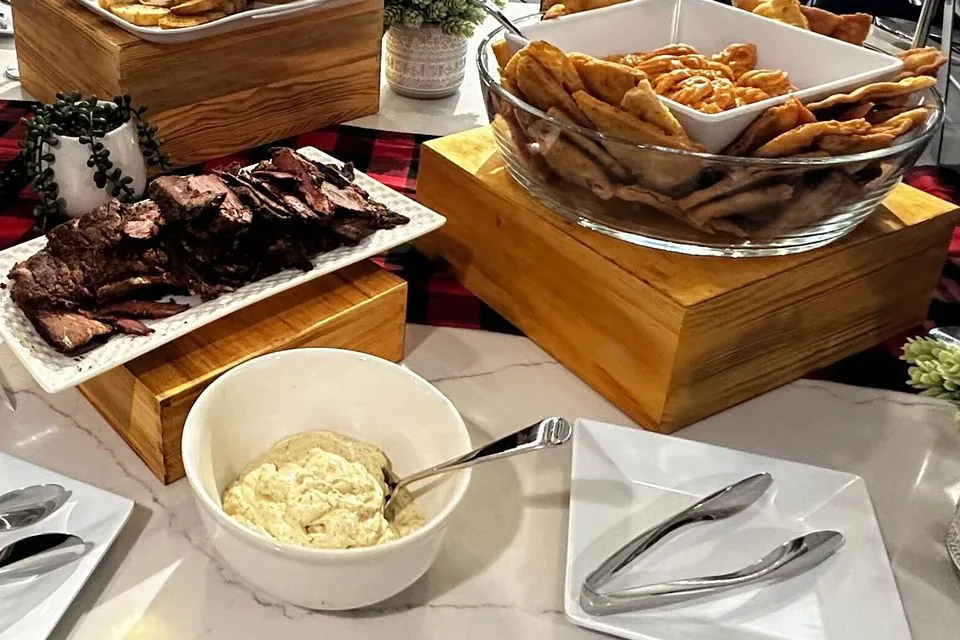Local barbecue caterer's office spread with sliced smoked tri-tip, potato salad, and pita chips on wooden risers