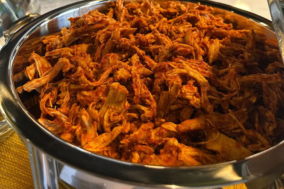 Saucy barbecue pulled chicken in a stainless chafing dish at an office catering buffet