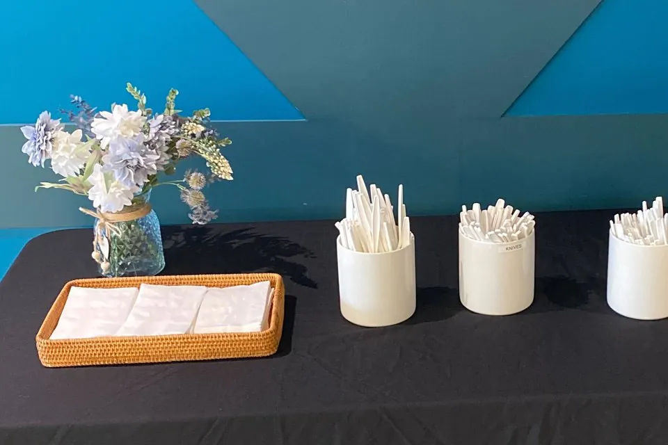 Napkin tray and three crocks of wrapped utensils on a black draped service table