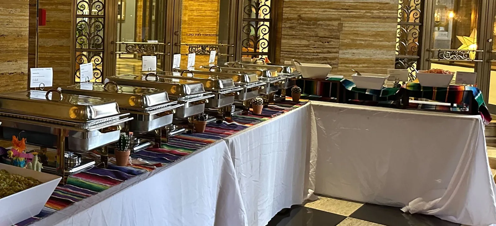 Catered buffet line with chafing dishes on draped tables in a historic event venue lobby