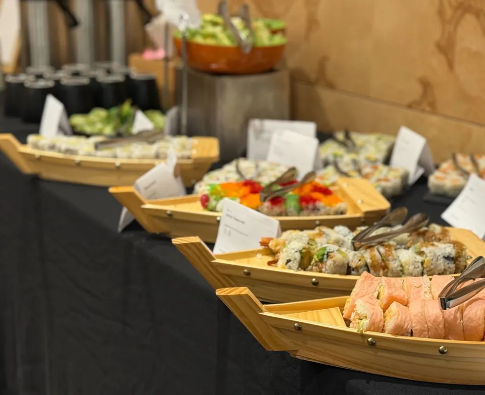 Sushi platters served in wooden boats along a black-linen catering table at an event