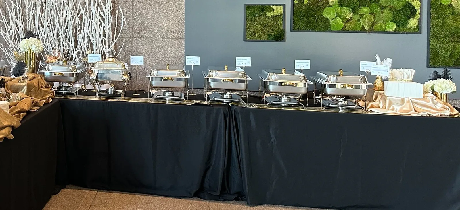 Office catering buffet with gold-trimmed chafing dishes of hot food on black draped tables