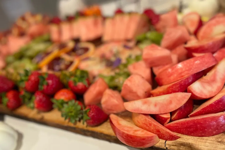 Large wooden grazing board with strawberries, watermelon, grapes, and apple wedges at an office catering spread