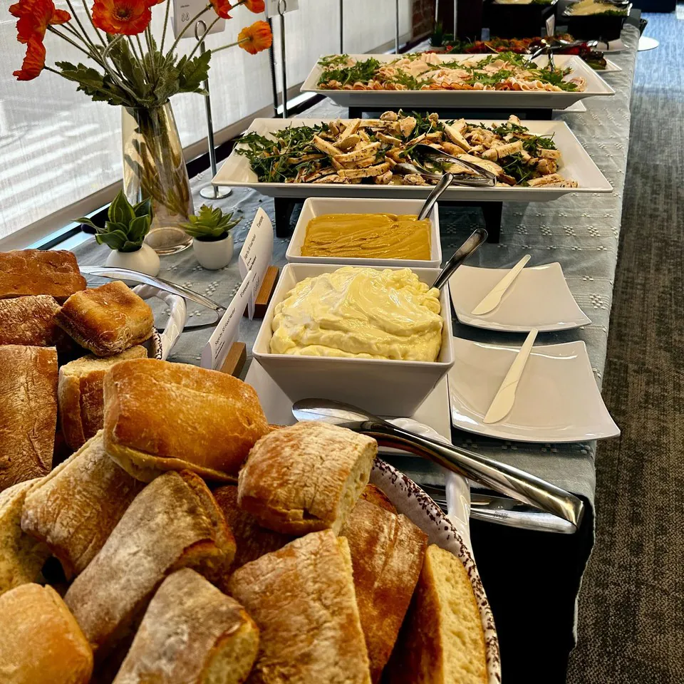 Office build-your-own sandwich bar with a basket of ciabatta, bowls of aioli and mustard, and platters of sliced grilled chicken and turkey