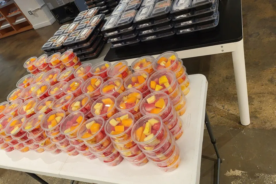Stacked individually packaged catering meals and lidded fruit cups staged on tables for an office delivery