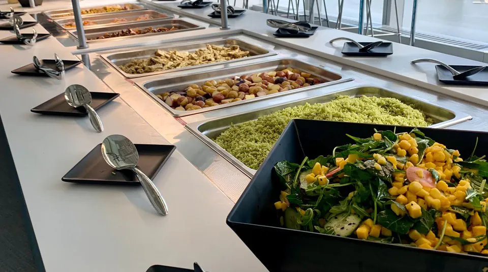 Office buffet line with greens, herbed rice, potatoes and grilled protein held in separate pans