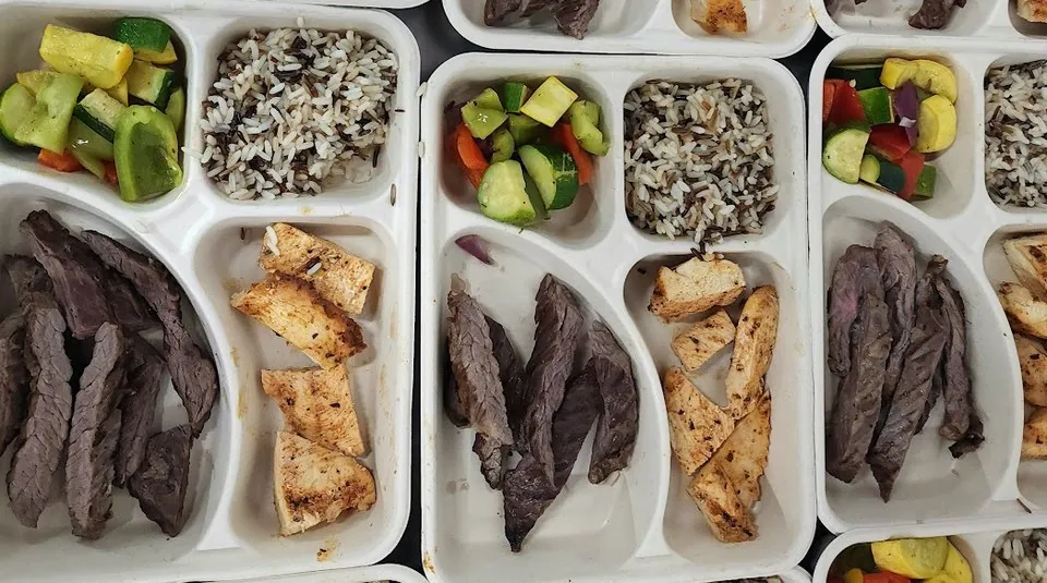 Compartment catering trays holding sliced steak, grilled chicken, wild rice and sauteed vegetables