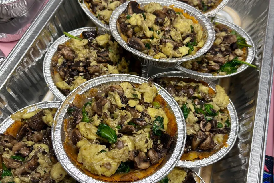 Individually portioned foil bowls of mushroom and spinach scramble lined up in a tray for a small office lunch