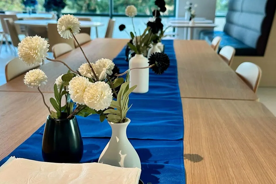 Office cafe tables set with runners, small floral vases and napkin caddies ready for a team lunch