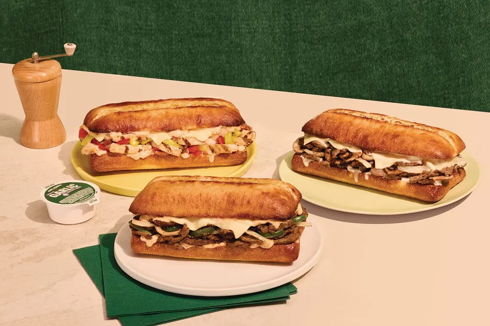 Three Papa John's oven-toasted ciabatta sandwiches onplates with a garlic dipping cup