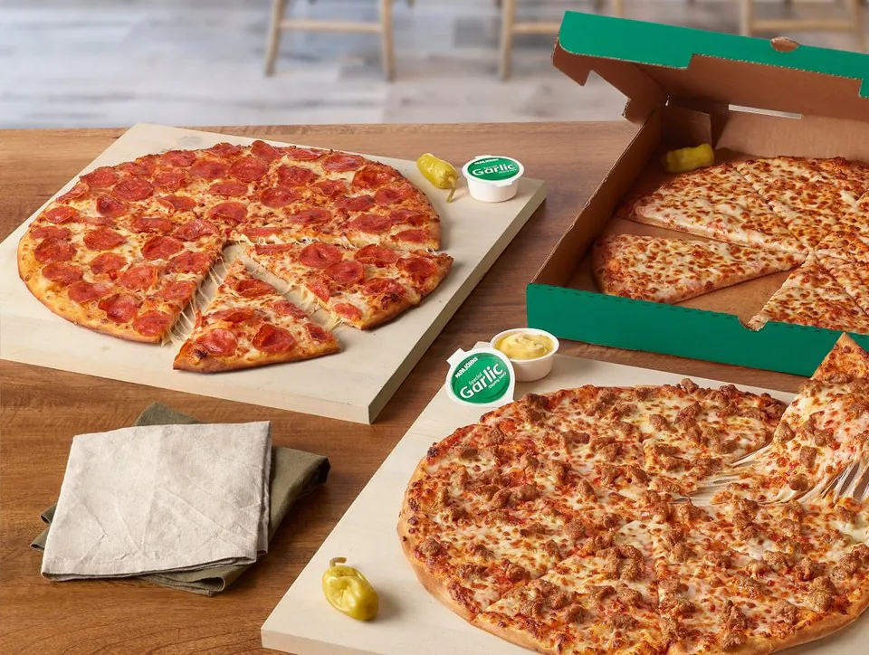 Three Papa John's pizzas on wooden boards beside an opendelivery box with garlic dipping cups