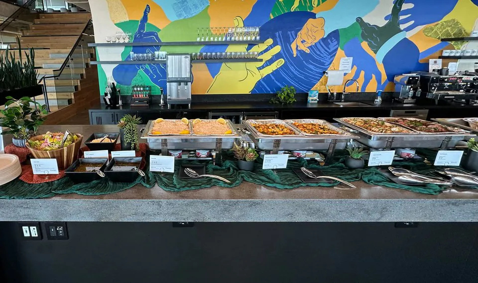 Office counter buffet with foil chafing trays, serving spoons and stacked plates