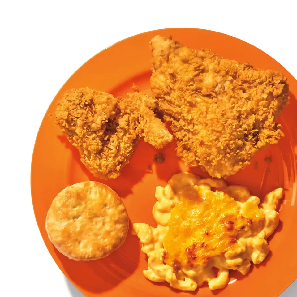Overhead view of an orange plate holding fried chicken pieces, a buttermilk biscuit and macaroni cheese