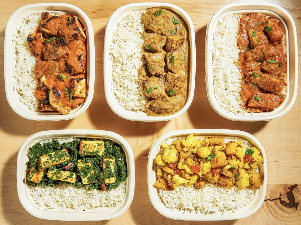 Five individually packed Rasa catering trays ofbasmati rice topped with butter chicken, lamb curry, chicken tikka masala, saagpaneer and spiced cauliflower and potato